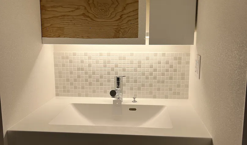 白いタイルの壁と下に白いシンク、上部に木製扉のあるミニマルな洗面台。