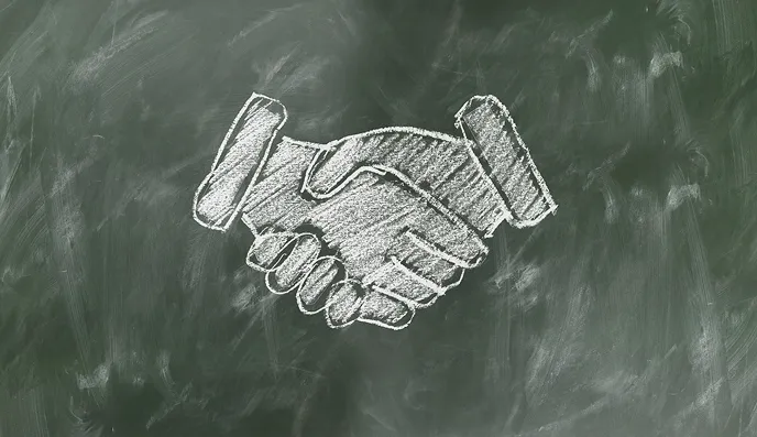 黒板にチョークで描かれた握手をする手のイラスト。