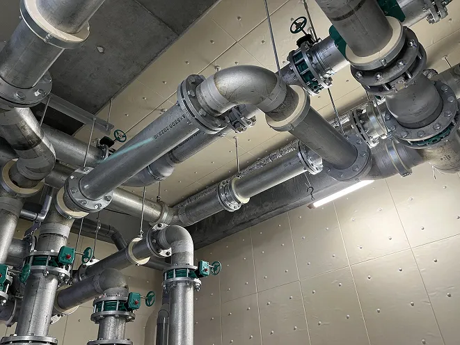 工場や施設の天井に取り付けられた複数の金属製パイプとバルブの配管システム。